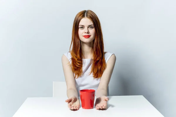 Schöne Frau am Tisch mit rotem Becher in der Hand bezaubert mit Lebensstil — Stockfoto