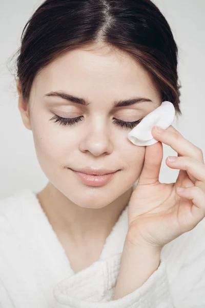 Vrouw in een badjas veegt haar gezicht met een zachte spons schone huid cosmetologie — Stockfoto