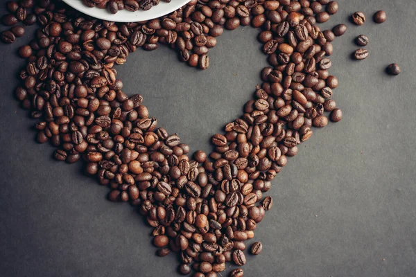 Corazón extraído de granos de café y una taza con un desayuno platillo bebida en la cama — Foto de Stock