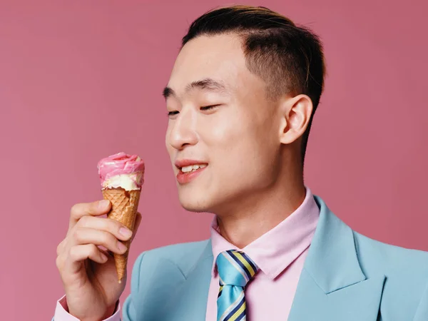 Egy jóképű férfi klasszikus öltönyben egy jégkrémet vizsgál rózsaszín alapon. — Stock Fotó