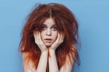 Üzgün kızıl saçlı, mavi arka planda dağınık saçlı, elleriyle el kol hareketi yapan bir kadın.