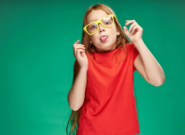 Χαρούμενα κόκκινα μαλλιά κορίτσι σε ένα κόκκινο μπλουζάκι κίτρινα γυαλιά συναισθήματα παιδική ηλικία — Φωτογραφία Αρχείου