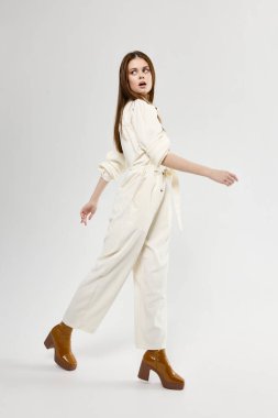 Şık bir tulum giymiş hoş bir kadın hafif arka planda ve kahverengi ayakkabılarla yan tarafa gidiyor.
