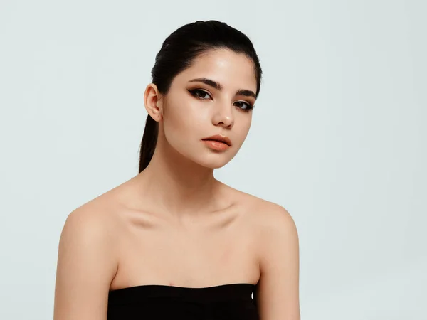 A pretty brunette in a black dress on a light background looks ahead — Stock Photo, Image