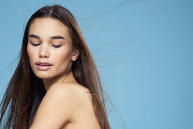 Güzel esmer, çıplak omuzlar uzun saç bakımı mavi arka plan