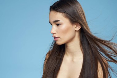 Güzel esmer, çıplak omuzlar uzun saç bakımı mavi arka plan