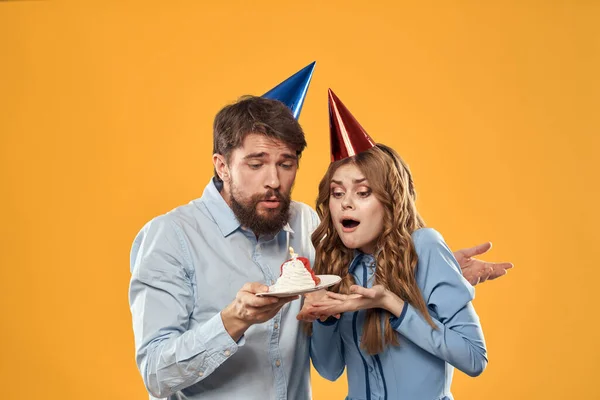 Anniversaire fête homme et femme dans une casquette avec un gâteau sur un fond jaune vue recadrée — Photo