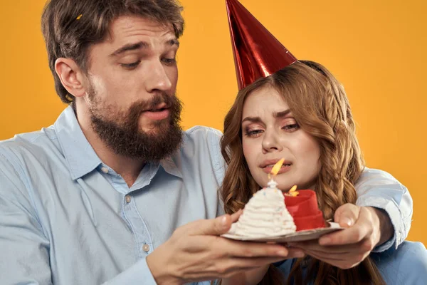 Aniversário festa homem e mulher em um boné com um bolo em um fundo amarelo vista cortada — Fotografia de Stock