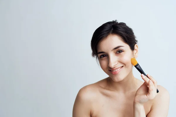 Pretty brunette with bare shoulders applying makeup to her face for an attractive look — Stock Photo, Image