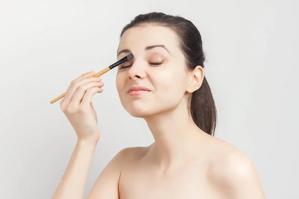 Morena bonita com um pincel em suas mãos aplicando procedimentos de maquiagem skincare — Fotografia de Stock