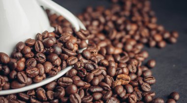 Beyaz fincan ve çay tabağı ve koyu arka plan makro fotoğrafında büyük kahve çekirdekleri.