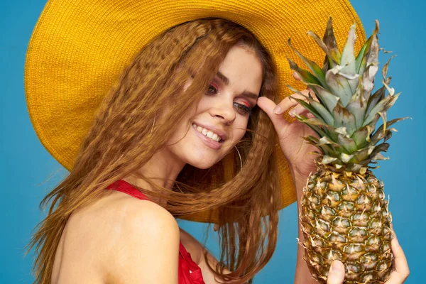 Kvinna i gul hatt med ananas händer lockigt hår exotiska frukter blå bakgrund attraktiv look — Stockfoto