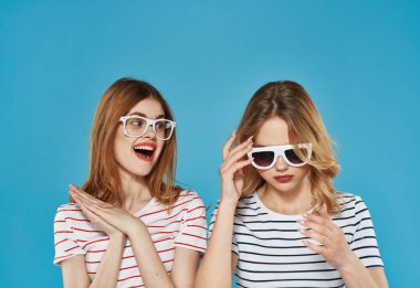 Çizgili tişörtlü iki neşeli kız arkadaş. Güneş gözlükleri, arkadaşlığa sarılıyor. 