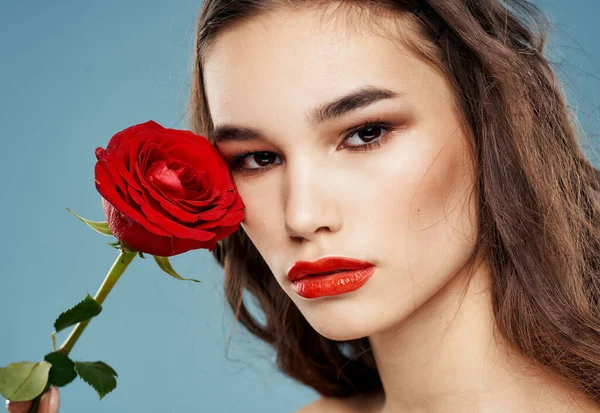 Une femme tient dans sa main une fleur rouge sur un fond bleu et du maquillage sur son visage — Photo