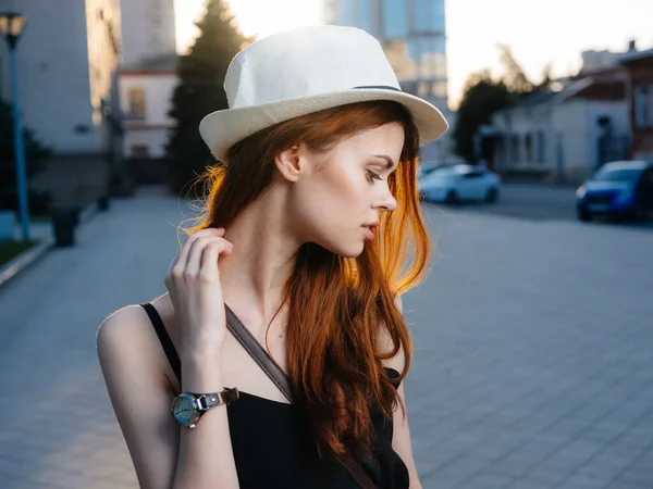 En vacker kvinna med rött hår i vit hatt och i svart klänning på gatan i staden — Stockfoto