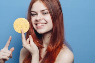 Neşeli kızıl saçlı, çıplak omuzlu, yüzü süngerle temizlenmiş bir kadın.