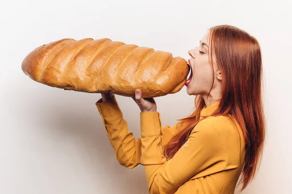 Woman eating a large loaf on a light background and a yellow shirt red hair model — Stock Photo, Image