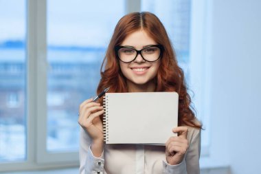 Beyaz tişörtlü, elinde not defteri olan kadın.