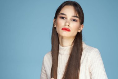 Beyaz süveterli esmer, kırmızı dudaklı, mavi manzaralı.