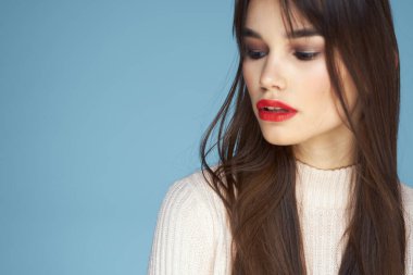 Beyaz süveterli esmer, kırmızı dudaklı, mavi manzaralı.