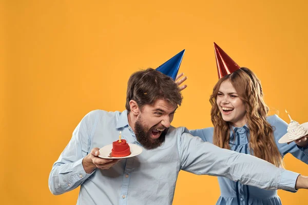 Fiesta de cumpleaños hombre y mujer en una gorra con un pastel sobre un fondo amarillo vista recortada — Foto de Stock