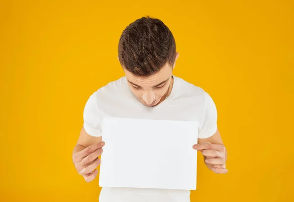 Een man in een wit T-shirt met een vel papier op een gele achtergrond — Stockfoto