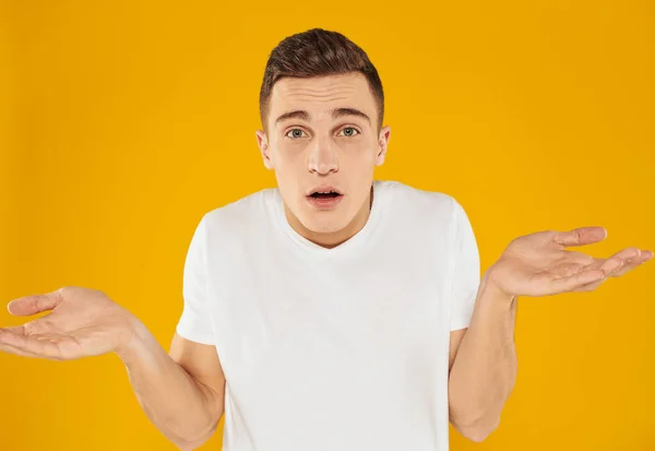 Emotional guy in a white T-shirt on a yellow background gestures with his hands portrait close-up beautiful face — Stock Photo, Image