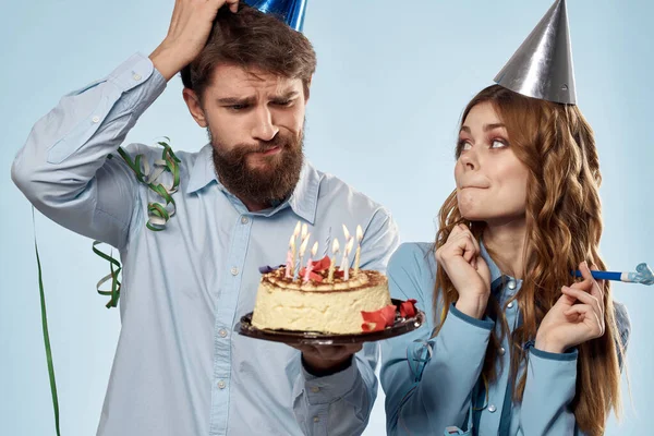 Homem de aniversário mulher em chapéus de festa em um fundo azul e bolo com velas — Fotografia de Stock