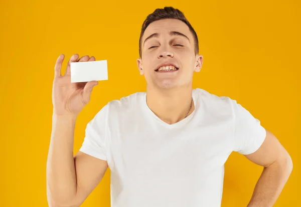 Chico en camiseta blanca que muestra la tarjeta de visita en el fondo amarillo vista recortada — Foto de Stock