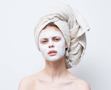 Kafasında havlu olan güzel bir kadın. Çıplak omuzlar ve yüzünde maske.