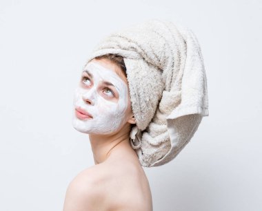 Kafasında havluyla mutlu bir kadın. Çıplak omuzları nemlendirici, yüz maskesi.