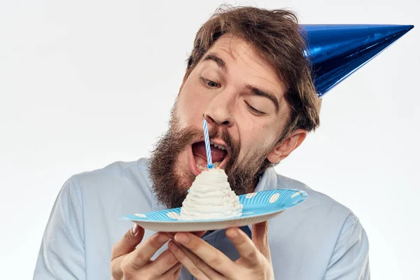 Un hombre con un plato de pastel y una camisa azul sobre un fondo claro fiesta de cumpleaños gorra corporativa — Foto de Stock