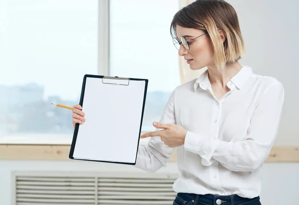 Eine Frau hält einen Ordner mit einem weißen Blatt Papier und einem Fenster im Hintergrund — Stockfoto