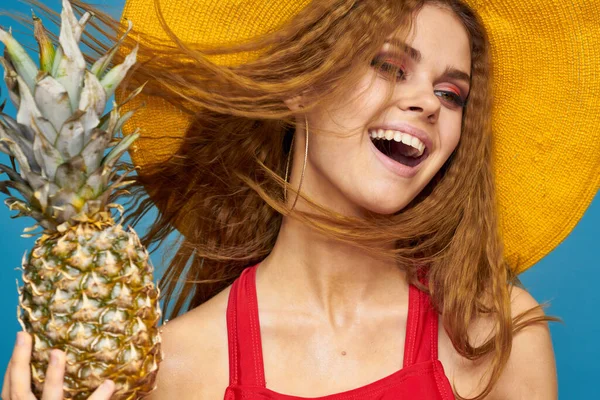 Kobieta w żółtym kapeluszu z ananasem ręce kręcone włosy egzotyczne owoce niebieski tło atrakcyjny wygląd — Zdjęcie stockowe