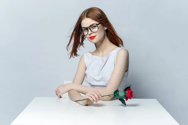 Roztomilá zrzavá žena sedící u stolu s růžovým květem v ruce okouzlující model — Stock fotografie