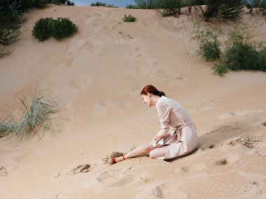 Açık renk elbiseli ve deniz kenarındaki kumsalda kırmızı sandaletli bir kadın.