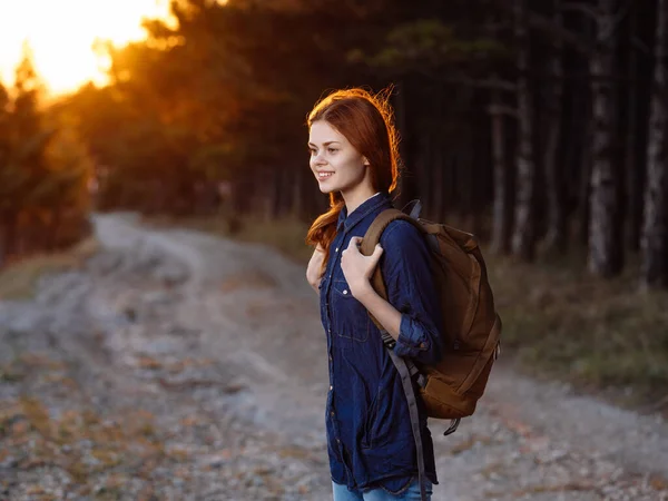 Woman on the road with a sunset sun backpack and forest in the background