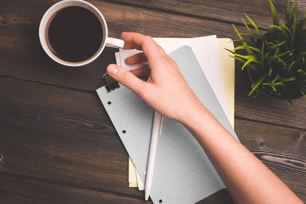 Жінка з чашкою кави в руці, сидячи за столом офіс блокнот аркушів паперової ручки — стокове фото