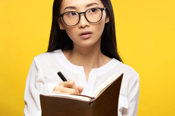 Elegantní žena v brýlích s poznámkovým blokem v ruce výuka student žluté pozadí — Stock fotografie