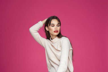 Uzun saçlı, kırmızı dudaklı beyaz bluzlu, pembe arka planlı çekici bir kadın.