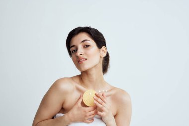 Beyaz havlulu, çıplak omuzlu bir kadın ellerinde süngerle cilt temizliği yapıyor.