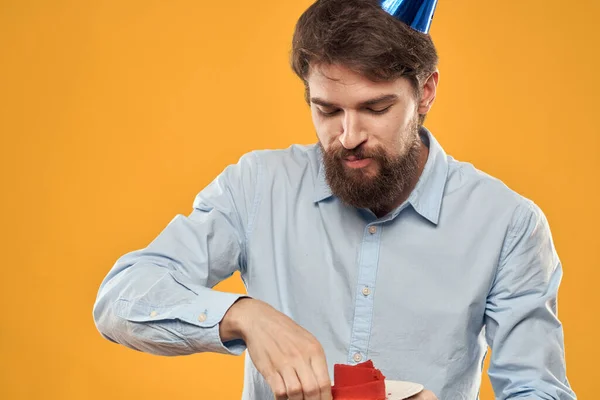 Man with cake on yellow background birthday party hat cropped view