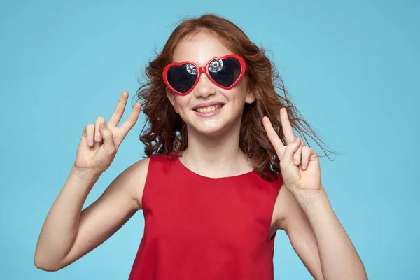 Маленька дівчинка в сонцезахисних окулярах у вигляді сердець червона сукня кучеряве волосся синій фон — стокове фото