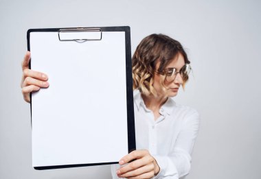 İş kadını elinde bir klasör tutuyor. Arka planda beyaz bir çarşaf var.