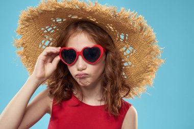 Plajda hasır şapkalı, güneş gözlüklü, kıvırcık saçlı, eğlenceli mavi arka planlı bir kız.