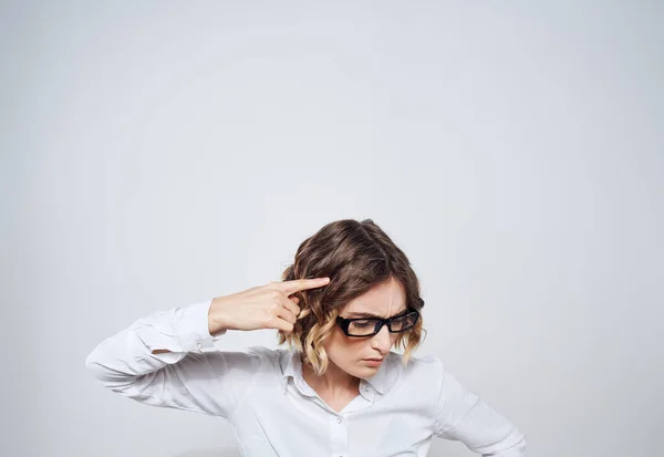 Eine Frau mit Brille und weißem Hemd berührt ihren Kopf mit den Händen vor hellem Hintergrund — Stockfoto