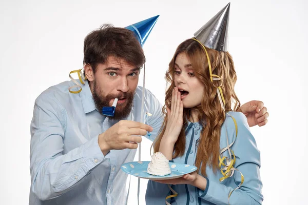 Energetic man and woman with a cake and in hats celebrate a birthday on a light background — Stock Photo, Image