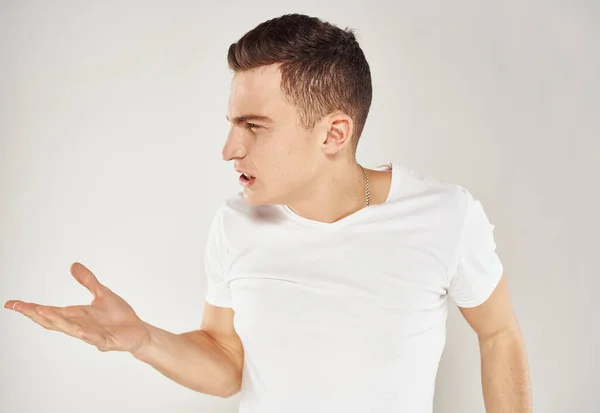Un homme en t-shirt blanc fait des gestes avec les mains sur un fond gris stress irritabilité — Photo