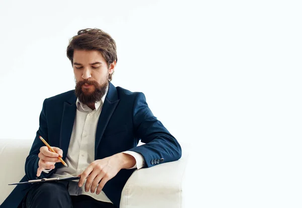 Un homme d'affaires dans un costume avec des documents dans ses mains sur un uniforme connecté assis sur un canapé à l'intérieur — Photo