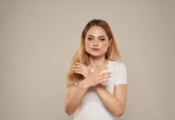 Kvinna i vit t-shirt på beige bakgrund kramar sig med händerna beskuren vy — Stockfoto